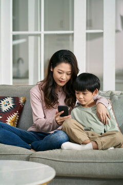 young asian mother sharing cellphone pictures with son at home