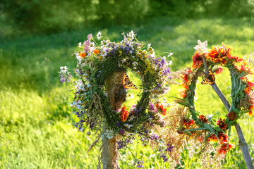 Fototapeta floral wreaths on wooden post, butterflies on meadow, sunny natural background. Floral crown, symbol of Summer Solstice Day, Midsummer holiday. witch tradition, wiccan ritual. Litha sabbat. obraz
