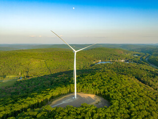 Afternoon aerial drone view of wind power turbines under construction, on a green forest. Wind turbines are part of the energy transition strategy	