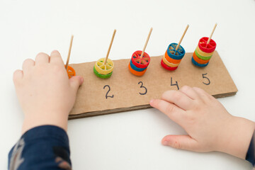 Home made tool for early education, fine motoric skills. 2 year old boy puts pasta on wooden rods. children, people, infancy and education concept. formation and development of the child.
