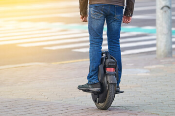Man on electric monowheel (EUC). Stylish guy moves along sidewalk on mono wheel. Man cross road on electric unicycle, commuting to work. Portable individual transportation vehicle. © Tricky Shark
