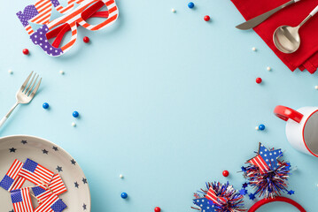 Fototapeta premium Show your American spirit with this table arrangement. Top view, including plate, cup, cutlery, napkin, sprinkles, headband, glasses, national flag on backdrop of pastel blue. Frame for text or promo