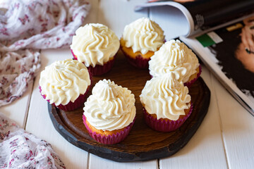 Sweet dessert for breakfast: delicious vanilla cupcakes with sweet delicate cream on a wooden stand. Sweet cake for breakfast. Close-up.
