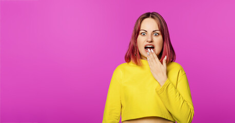 Amazed woman with pink hair looking desperately anxious and covering her mouth with hand, standing...