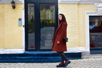 Young stylish woman walks down the street in a brown coat