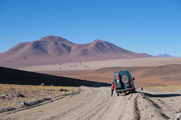 Woman in a red jacket leaning against a green campervan on a dusty road in Bolivia in the Eduardo Abaroa Andean Fauna National Reserve