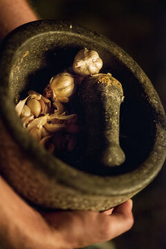 arms hold a large black traditional molcajete filled with garlic in low light
