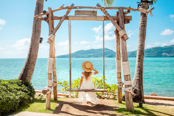 Relaxation and happiness of woman in a straw hat and white dress sitting on a swing with the...