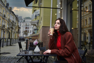 Dreaming Woman on the terrace sits at a table with a cup of coffee she is waiting for a friend