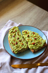 Turquoise plate with two pieces of avocado toast on wooden table. Selective focus.