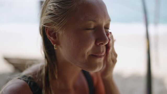 Blonde caucasian female surfer applying sunscreen on her face. Tanned young surfing woman putting spf on her cheeks, nose and forehead close-up. Portrait of surfer girl usinf spf skin protection