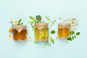 Jars with different types of honey on color background, top view