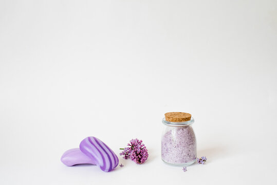 Spa care with natural soap, sea salt, washcloth glove for body care, lilac flowers and a candle on a light background with copy space