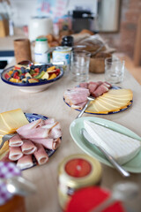 counter view of breakfast spread with lots of different types of fruit lunch meat ham cheese berries apples yogurt bread baguette, loaf, muffins, croissants, kitchen space natural neutral  european 