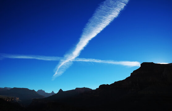 Jet streams in evening sky above the grand canyon, with canyon walls in silhouette.  Lots of copy space.