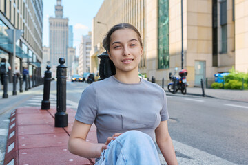 Young smiling teenage girl looking at camera on street of modern city