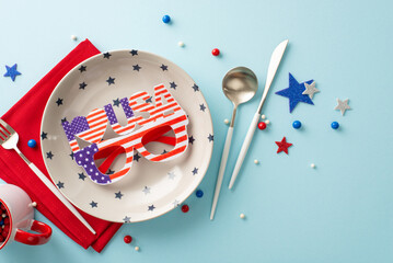 Fototapeta Fourth of July-inspired table setting. Overhead view of patriotic decor including party glasses in national flag colors, plate, cup, silverware, napkin, stars, round sprinkles on pastel blue backdrop obraz