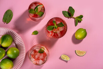 Strawberry mojito. Cocktail with rum, mint, lime and ice in a glass on a pink background. Homemade beverage.