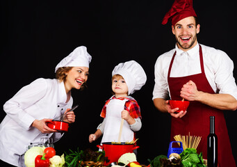 Happy family in chef uniform preparing breakfast, dinner or supper. Healthy food at home. Parents teaching little boy to cook. Mother, father and son cooking in kitchen together. Homemade food.