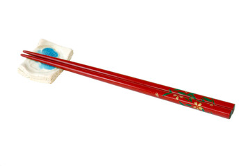 A set of red lacquered chopsticks with rest on a white background.