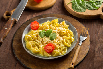 Pasta in a creamy sauce with cheese with a fork on a wooden stand next to tomatoes, a knife and greens