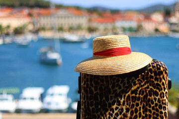 Stylish suitcase and straw hat outdoor. Idyllic Mediterranean town in the background. Summer...