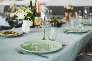 Wedding banquet. The festive table is decorated with compositions of flowers and greenery. On the table are glasses, talers with napkins, cutlery and name cards and menu cards.