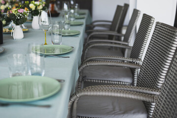 Wedding banquet. The festive table is decorated with compositions of flowers and greenery. On the table are glasses, talers with napkins, cutlery and name cards and menu cards.