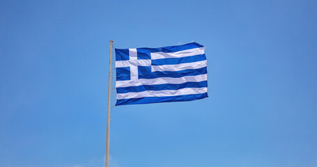 Greece. Greek national official flag on flagpole waving in the wind, blue sky