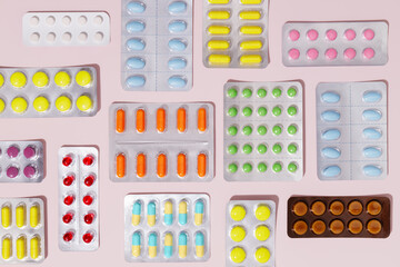 Pharmaceutical colorful pills and capsules packed in blisters on a pink background