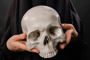 close-up of a human skull in the hands of a woman dressed in a black robe
