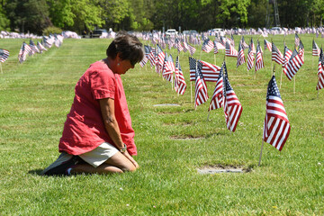 Woman grievingat gravesite of a loved one in a veterans cemetery with American flags in the background