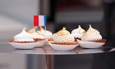 Sale of desserts and sweets at the French wine and food festival in Holesovice, Prague. Closeup of metal tray with mini tarts with flambé meringue and French tricolor, selective focus, no people. - obrazy, fototapety, plakaty