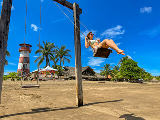LOW ANGLE VIEW Cheerful tourist having fun on beach swing in front of lighthouse