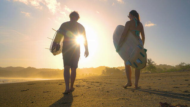 LENS FLARE: Surfers carry surfboards on a tropical sandy beach in golden light