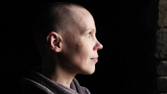 A bald woman looks out the window. Baldness after chemotherapy.