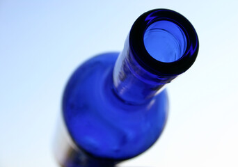 Blue bottle in the background of sky. Close-up. Some water drops on the neck