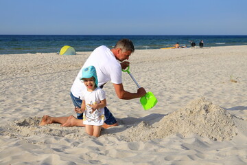 A small child playing with father on a sandy beach during a holiday on the Baltic Sea. The concept of traveling with children
