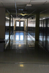 School hallway natural light from doors at the end leading outdoors, lined with lockers, and reflected light on tile floor.