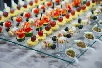 A variety of snacks and canapes are laid out on a glass table. Wickedly designed and laid out food. Holiday catering. Light back.