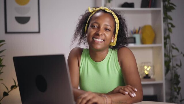 Video Young African woman using laptop computer in office. Happy girl poses looking camera and teleworking. Cheerful people sitting at desk in studio. Enterprising and hardworking person concept 