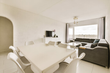 a living room and dining area in a house with white walls, floor tiles and large windows overlooking the sea