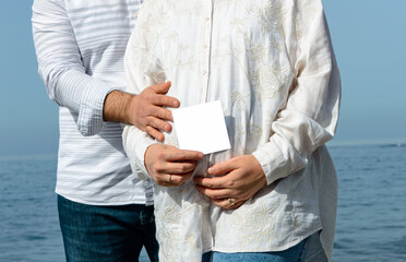 Pregnant woman and man holding hands with the white note paper with space for text.