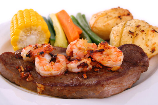 A steak with garlic butter sauce and fresh king prawns - surf n' turf, with fresh vegetables on a white plate