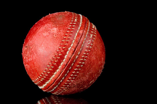 Red, scuffed Cricket ball on black background with reflection