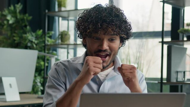 Surprised shocked amazed Arabian Indian Latino man ethnic male guy businessman astonish wonder surprise happy shock reaction win online project on laptop sucess shouting celebrate victory achievement