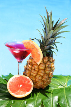 Tropical cocktail with fruit and blue water background; don't miss the wasp on the grapefruit garnish