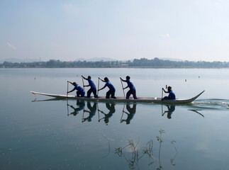 Four paddlers and a helmsman practicing early in the morning onboard a small dragonboat near...
