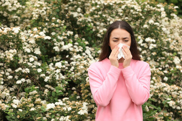 Woman suffering from seasonal pollen allergy near blossoming tree on spring day