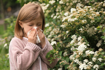 Little girl suffering from seasonal pollen allergy near blossoming tree on spring day
